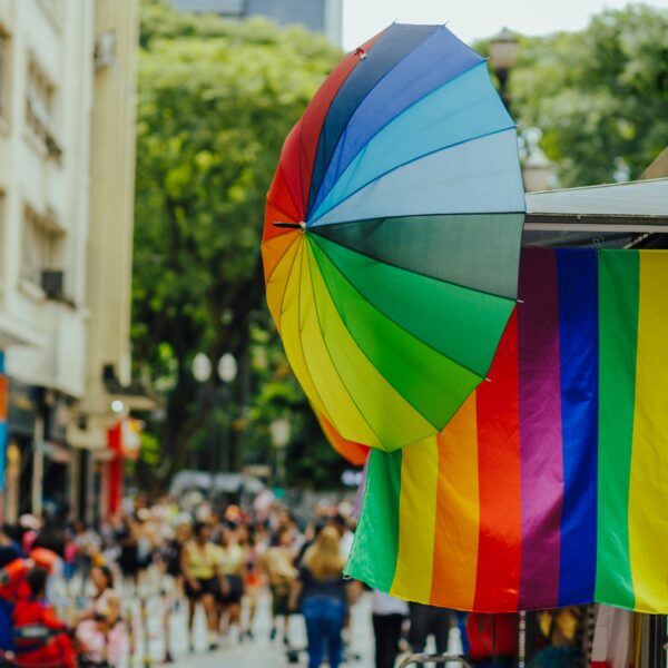 Colorful street scene with a rainbow umbrella and flag, capturing vibrant energy and diverse crowd.