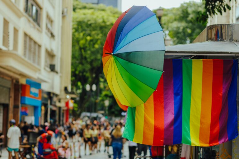 Colorful street scene with a rainbow umbrella and flag, capturing vibrant energy and diverse crowd.