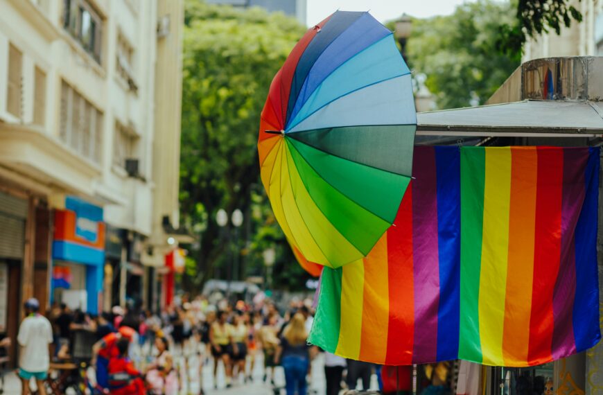 Colorful street scene with a rainbow umbrella and flag, capturing vibrant energy and diverse crowd.